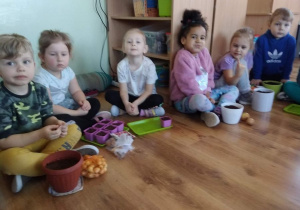 Dzieci siedzą na podłodze, gotowe do posadzenia cebulek
